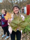A woman holds two huge leaves and smiles 