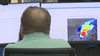A man works in front of two computer monitors. The right screen shows a storm tracker