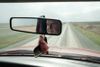 A farmer's face is reflected in a rearview mirror as he drives along a rural road between fields near Palo, Iowa.