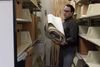 A man carries a bundle of large papers between the shelves of an archive