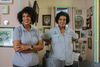 Two women wear shirts with "The Descendants Project" logo. The walls behind them are filled with framed antique portraits
