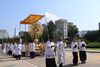A procession of people in traditional catholic garments move a large golden sun-shaped statue down a street