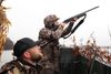 Friends Brett Hanson and Jordan Lillemon hunt ducks together, one aims his shotgun skyward while the other stands nearby, watching.