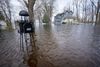 A wire mailbox stands in the foreground out of floodwater that covers a neighborhood. A house in the background is mostly protected from the water by a tall foundation 