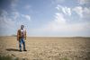 A man stands in jeans and a jacket as he looks out over a vast yellow field