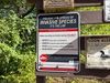 A metal sign in a wooded area tells boaters of their responsibilities to stop the spread of invasive aquatic species.
