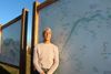 A woman with white hair stands by a large map of the Mississippi River outside in the sunlight 