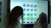 two female scientists in lab coats look at medical images on a screen