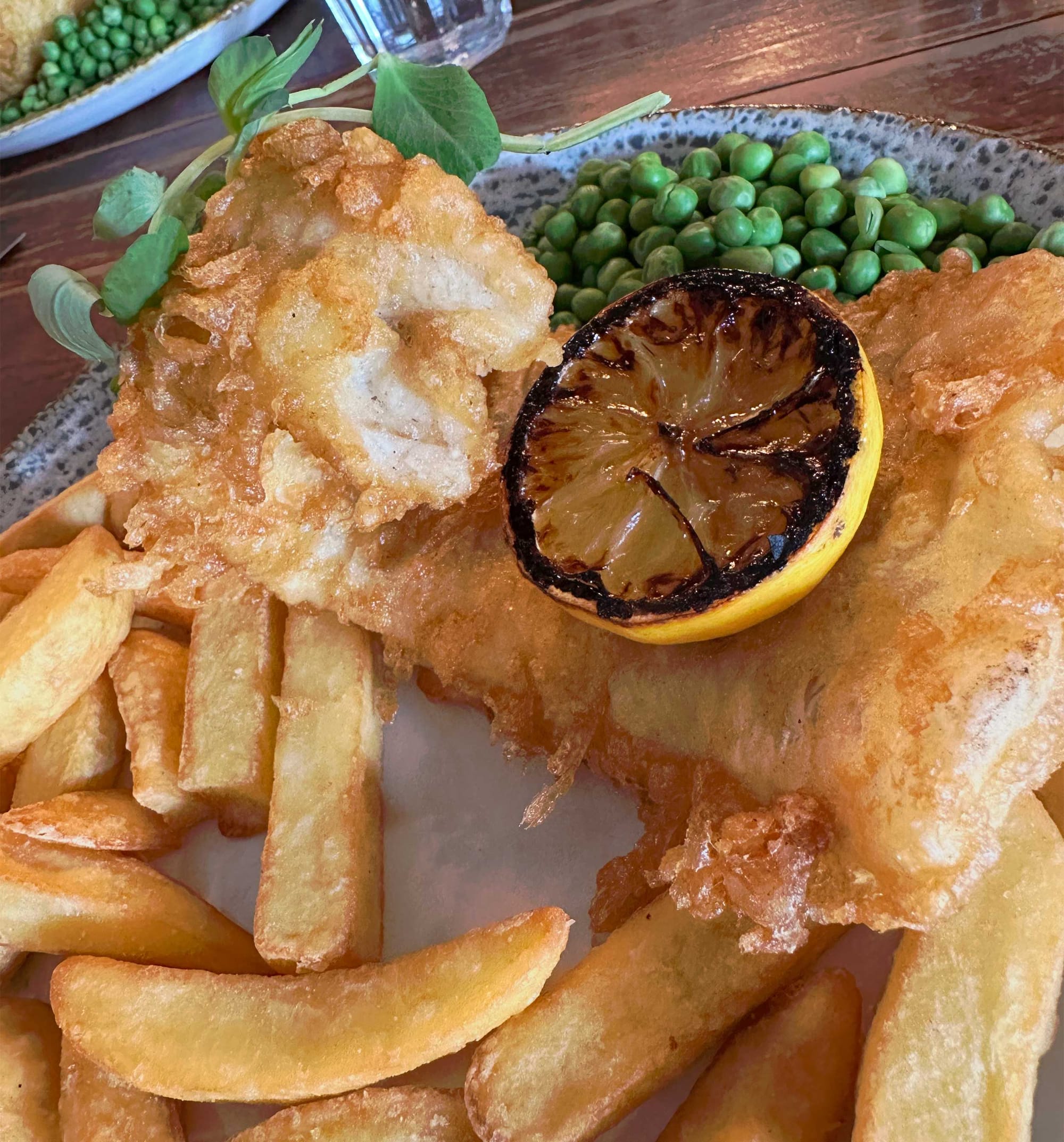 Fish, French fries, peas and a lemon on a plate.