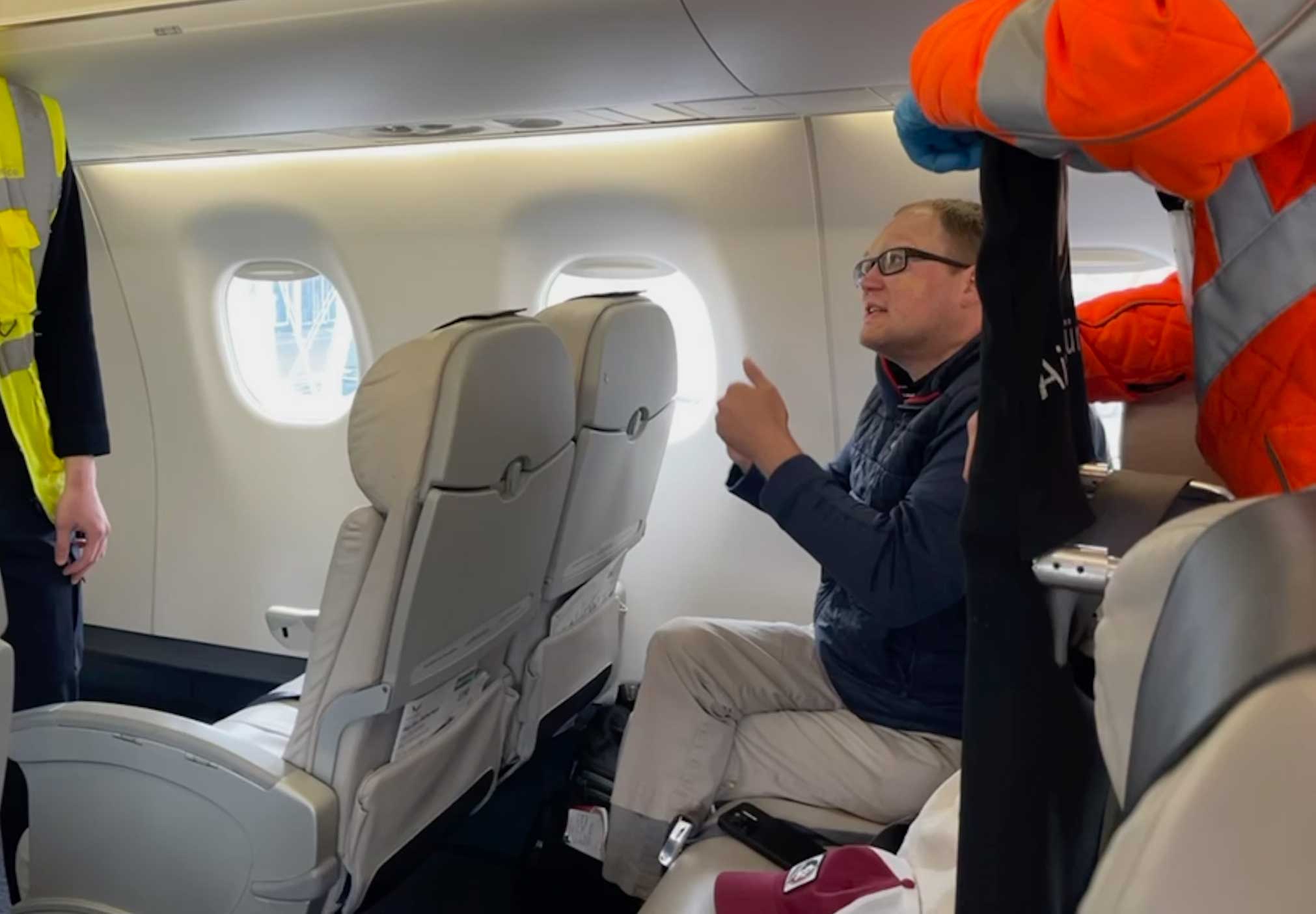 John seated on board an airplane making a point to two airport employees.