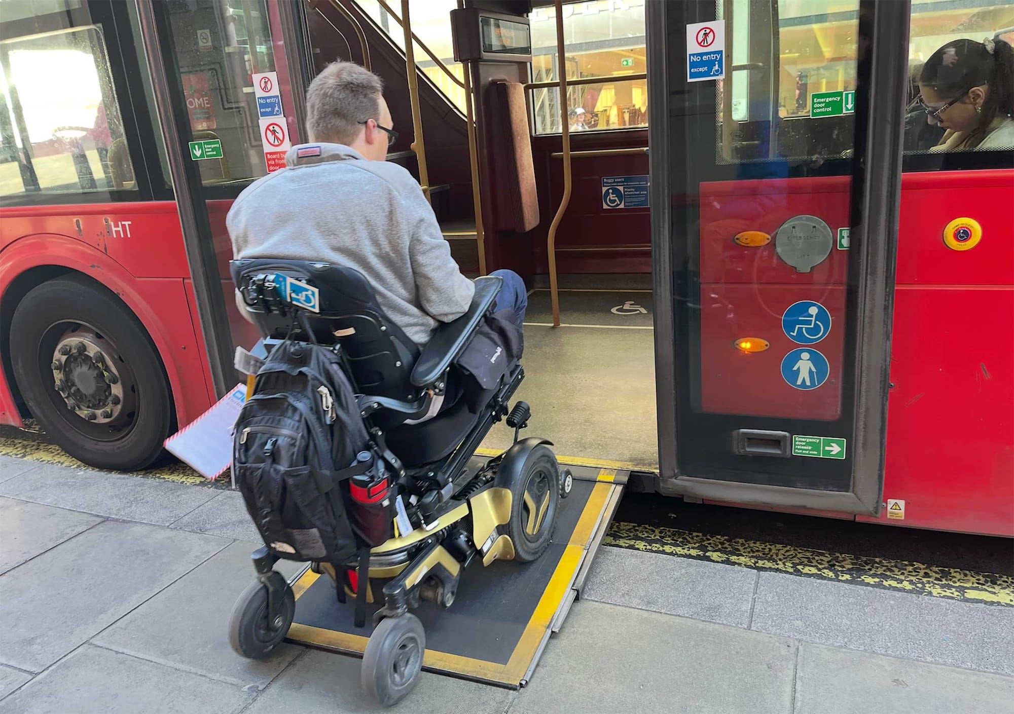 John seated in his wheelchair going up the ramp to a red London city bus.