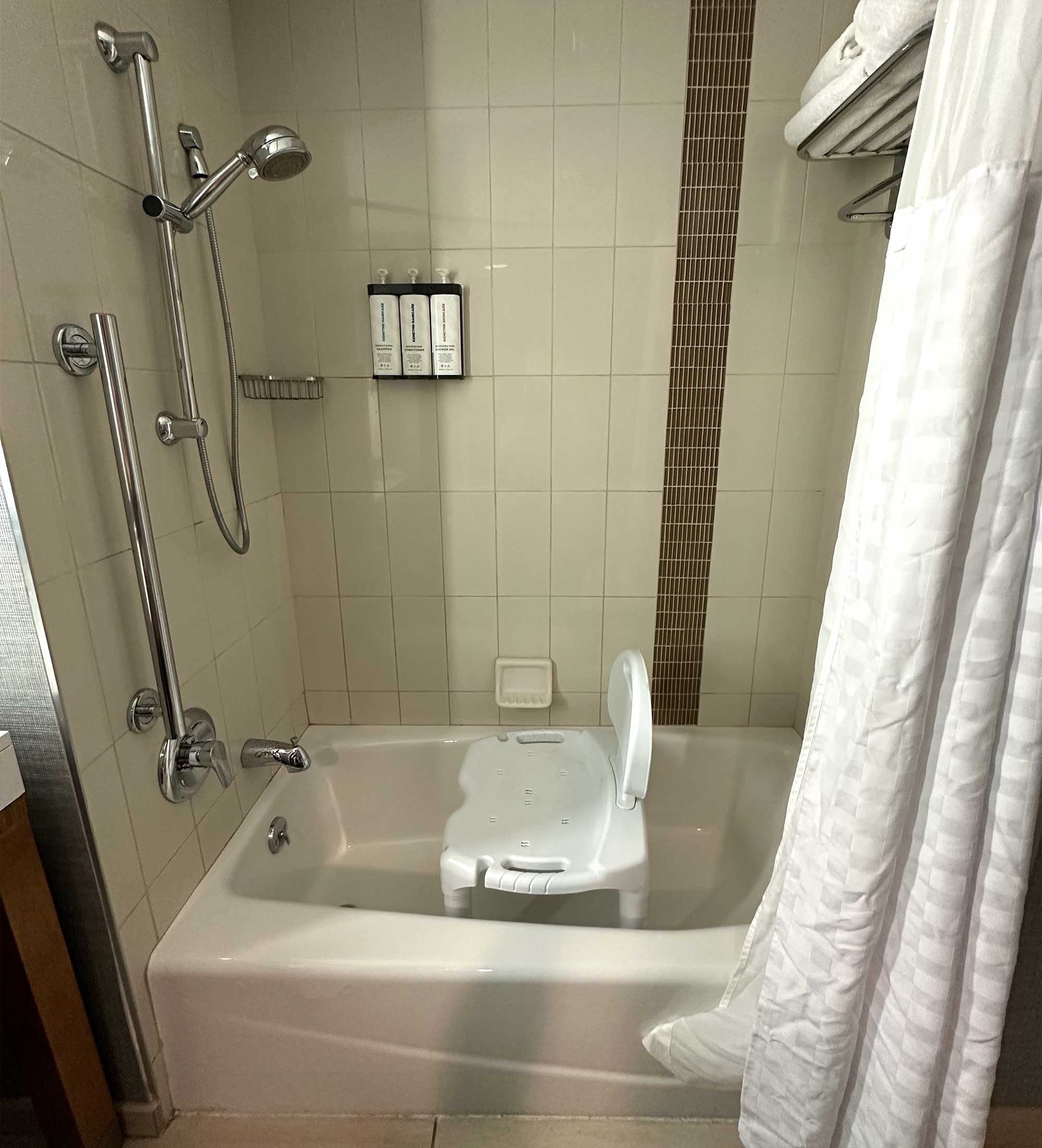 Bathtub without grab bars and a portable shower seat inside.