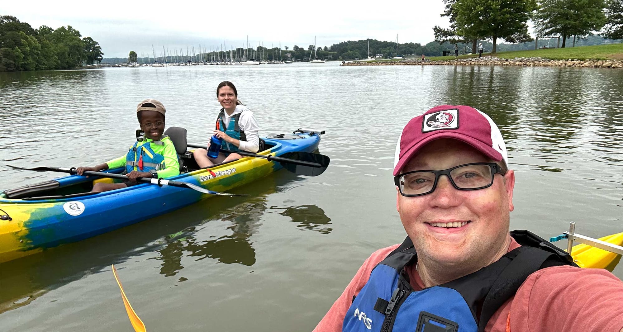 Selfie of John in a kayak next to Stevie and Robert in a kayak on the water.