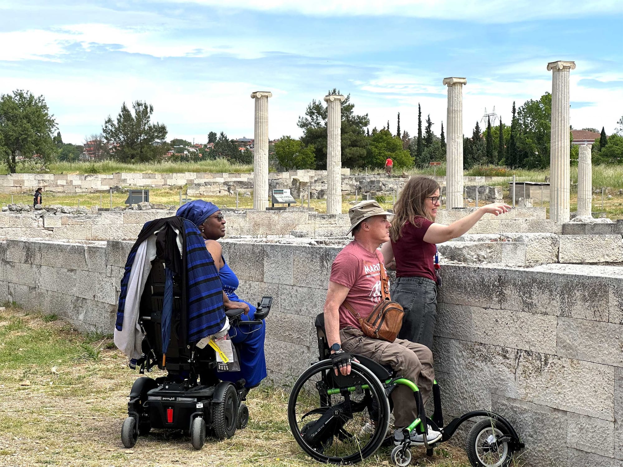 Wheelchair users with tour guide amidst ancient ruins.
