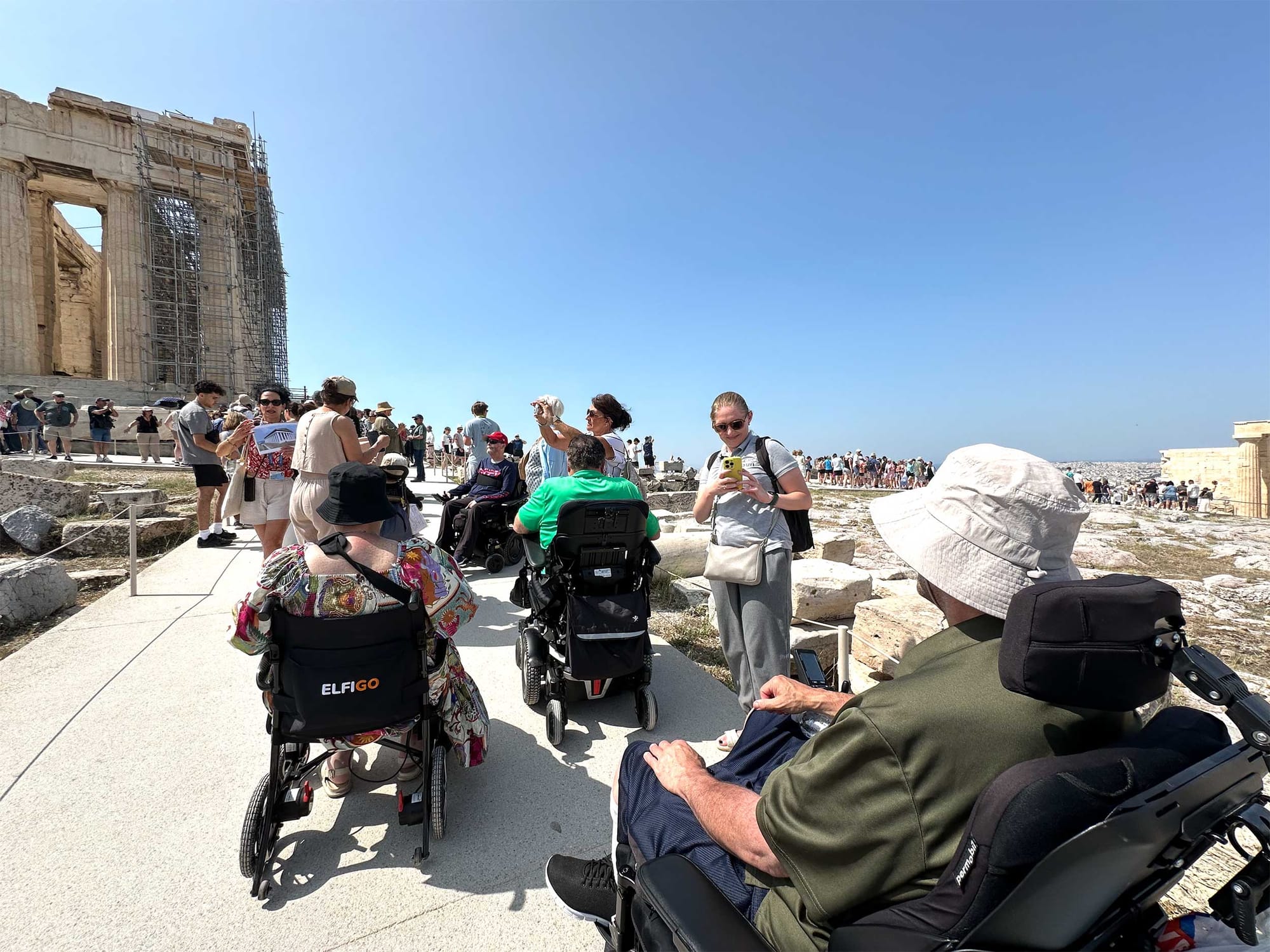 Group of wheelchair users moving on a sidewalk towards the Parthenon.