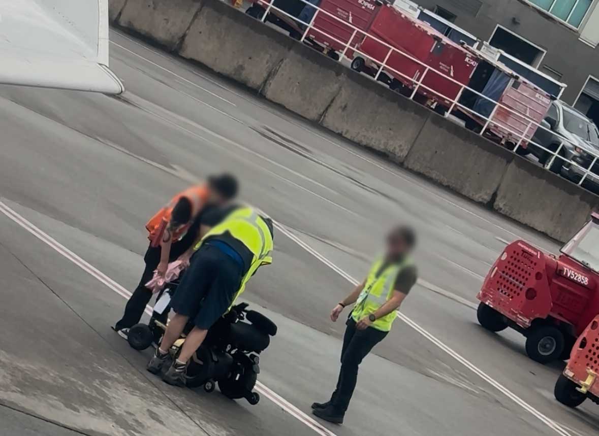 Airline staff drying off a wet power wheelchair with towel.