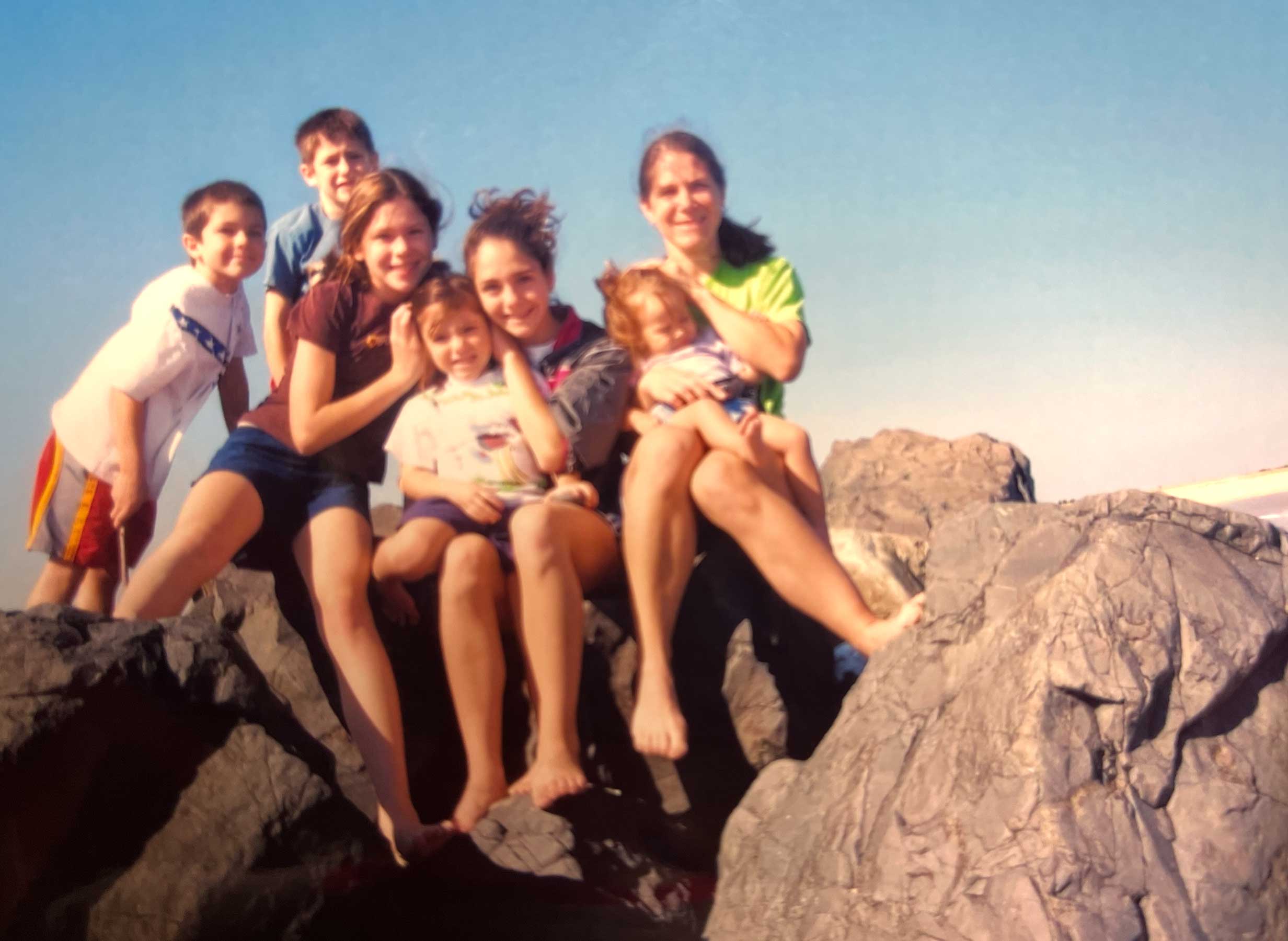 Stevie as a child with her brothers, sisters and mom seated on a rock formation at the beach.