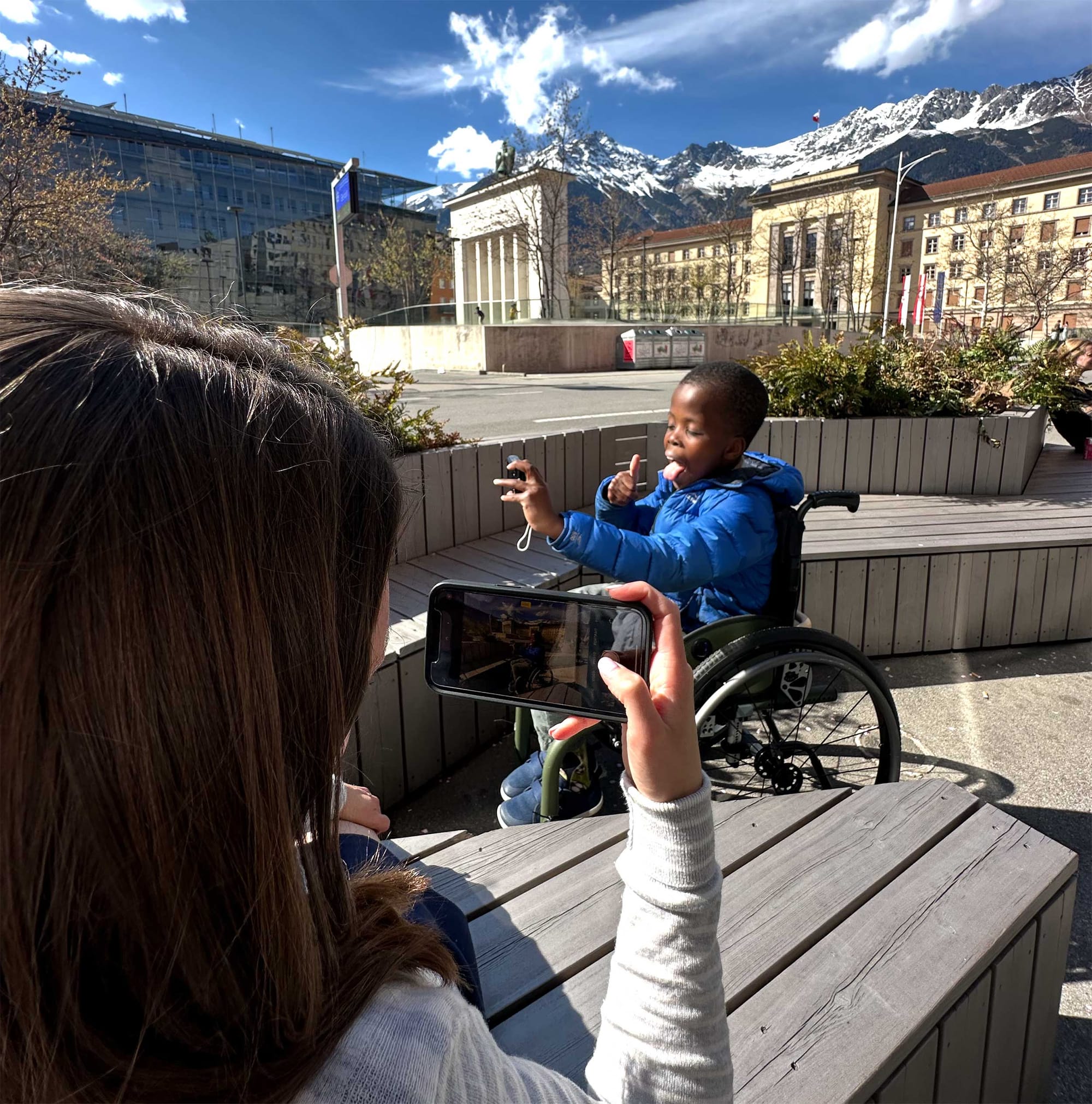 Stevie taking a photo of Robert taking a selfie of himself against the backdrop of a city skyline and mountains in Austria.