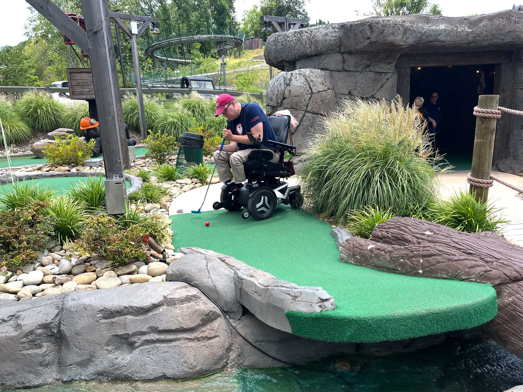 John sitting in his wheelchair lining up a putt on the miniature golf course.