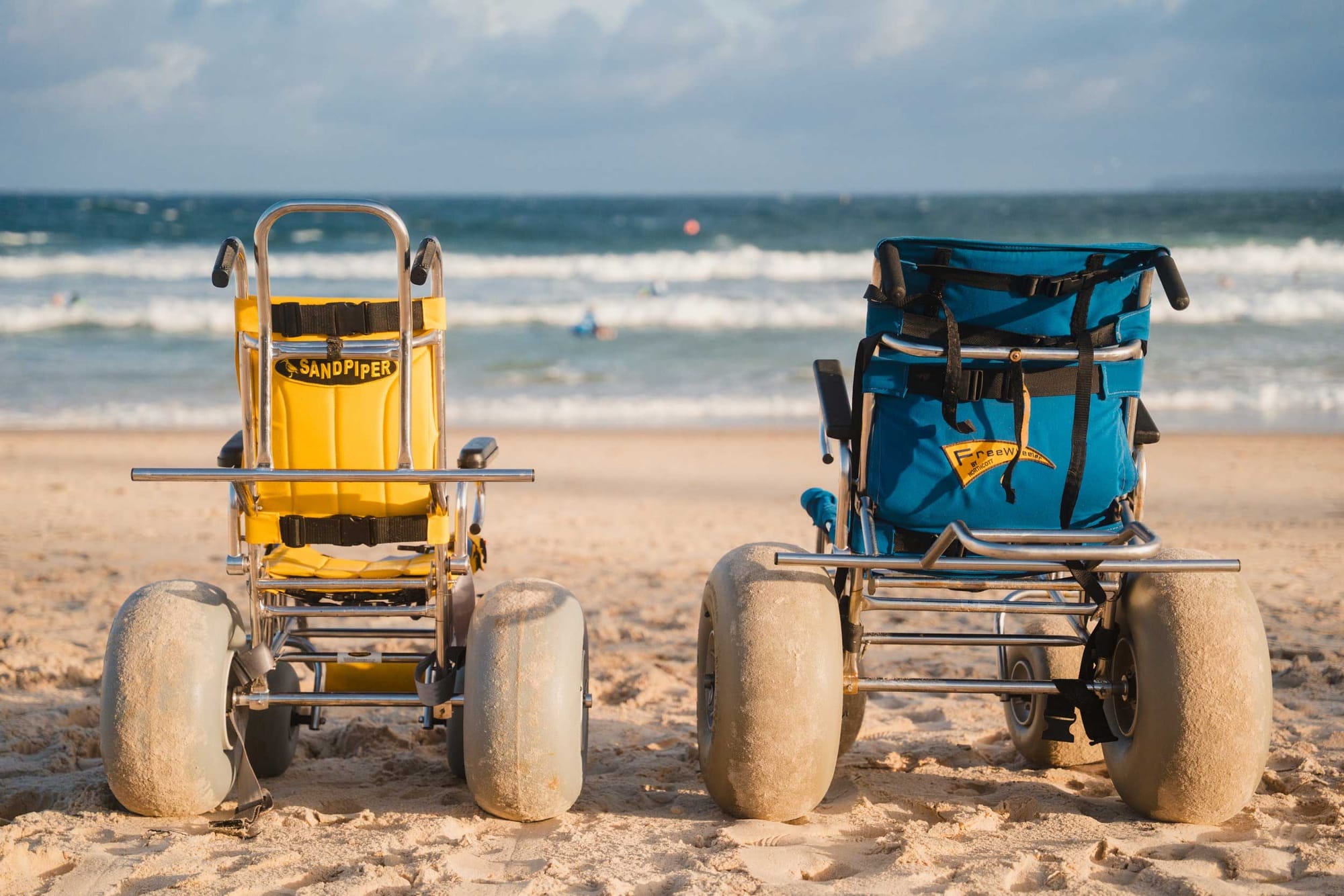 Two beach wheelchairs on a sandy beach.