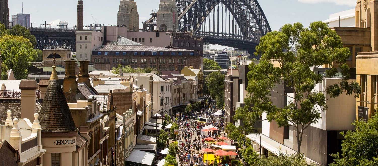 Overhead view of harbour bridge and street filled with pedestrians.