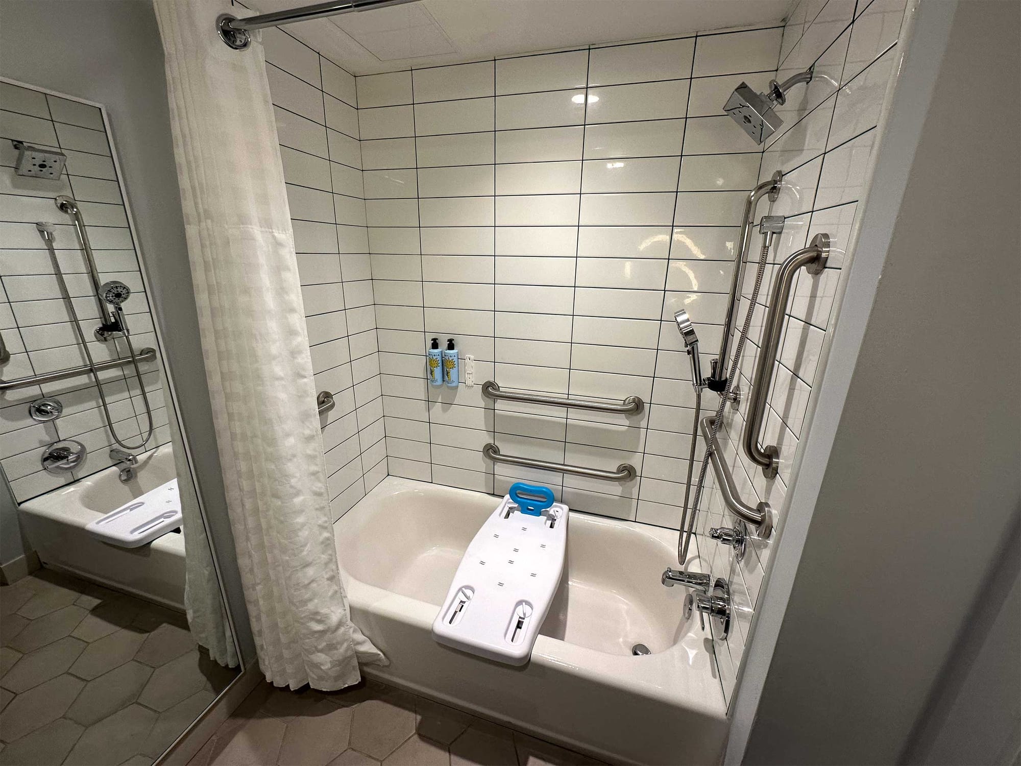 Bathtub with grab bars, seat and an adjacent floor length mirror.