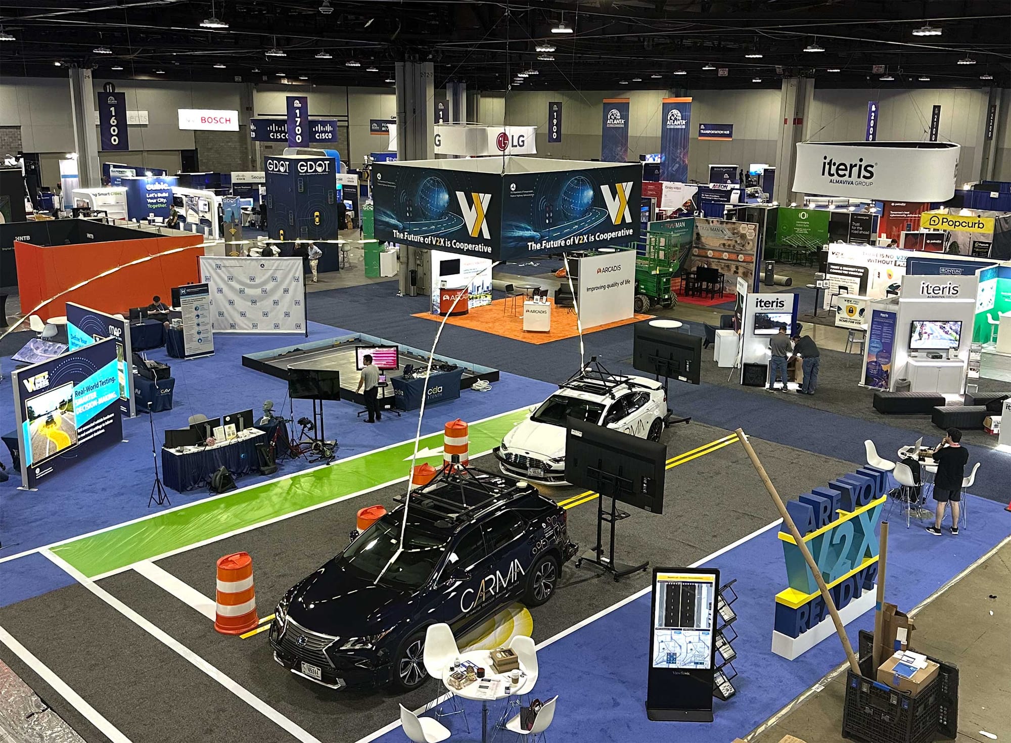 Overheard view of one of the exhibit floors at conference, with booths, cars and other displays.