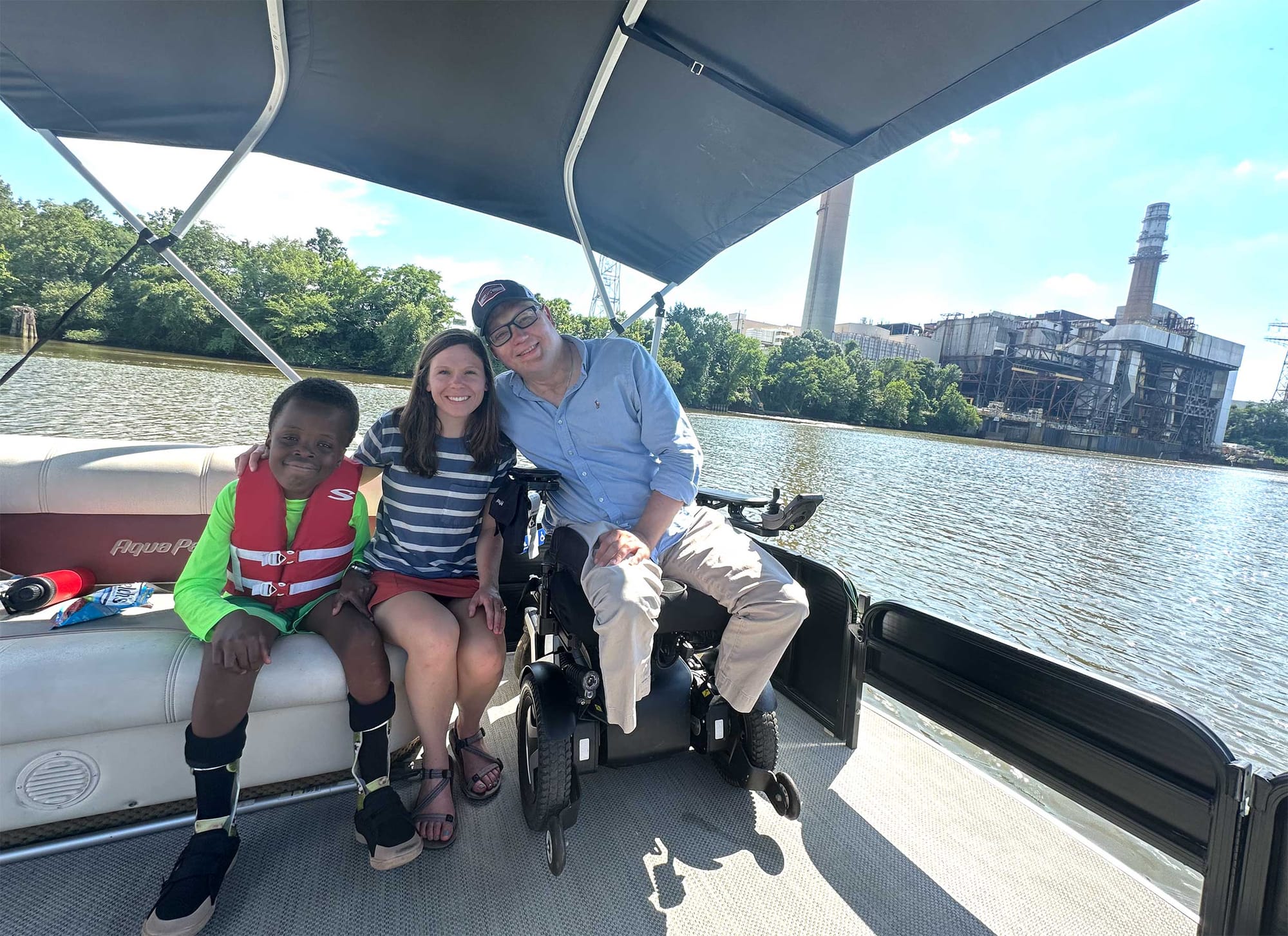 Stevie, John and Robert on a boat on the river, passing by a large factory or power station.