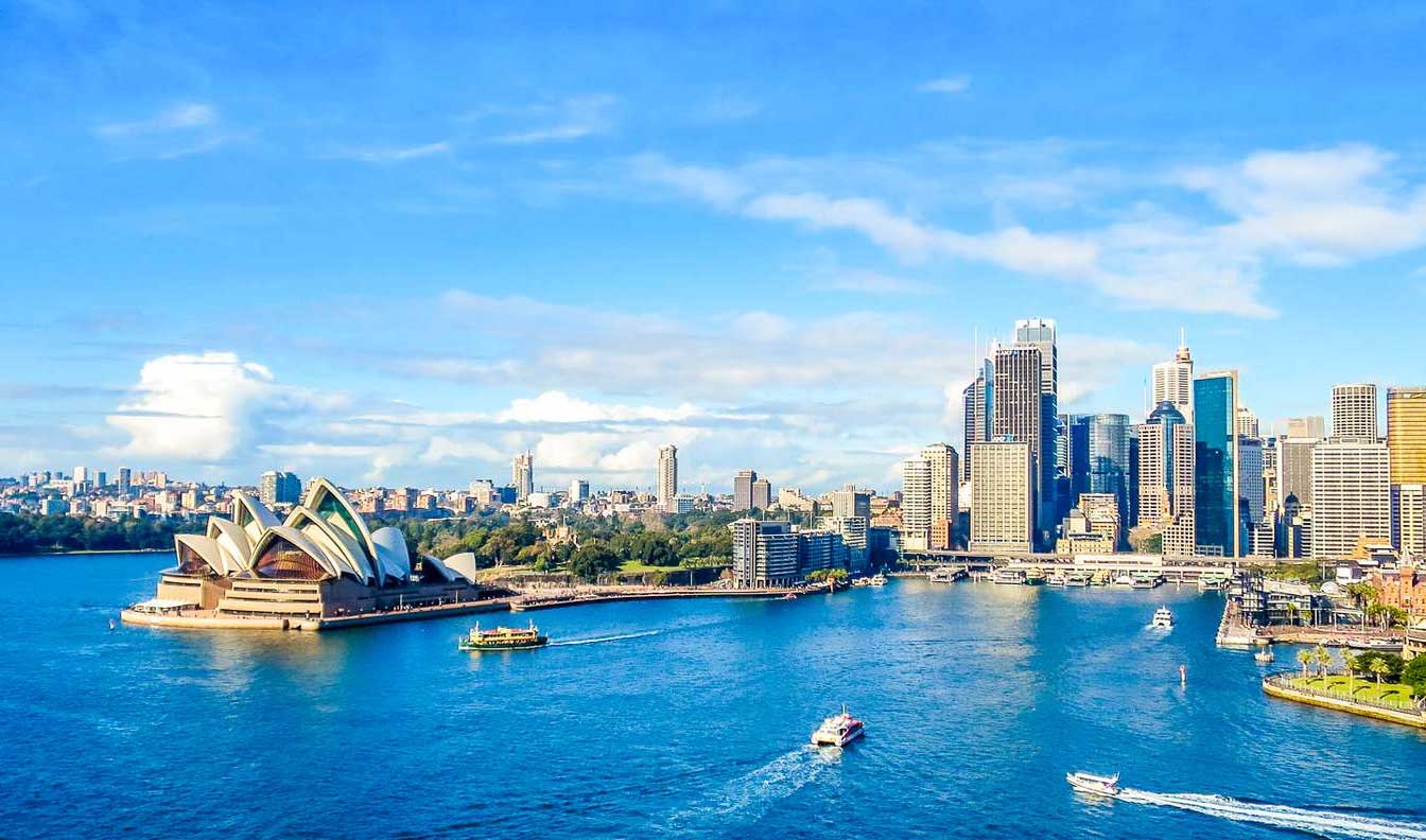 Sydney Harbor with ferries on the water and the opera house in the foreground.