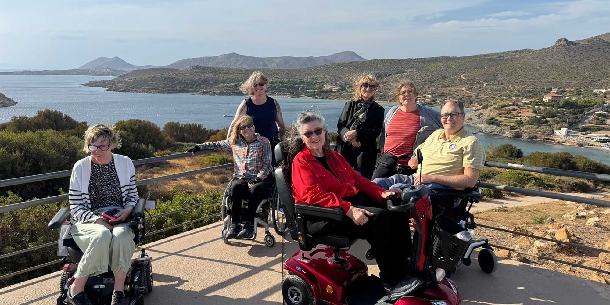 John pictured with six Wheelchair Travel readers, all women, in front of the Greek coastline.