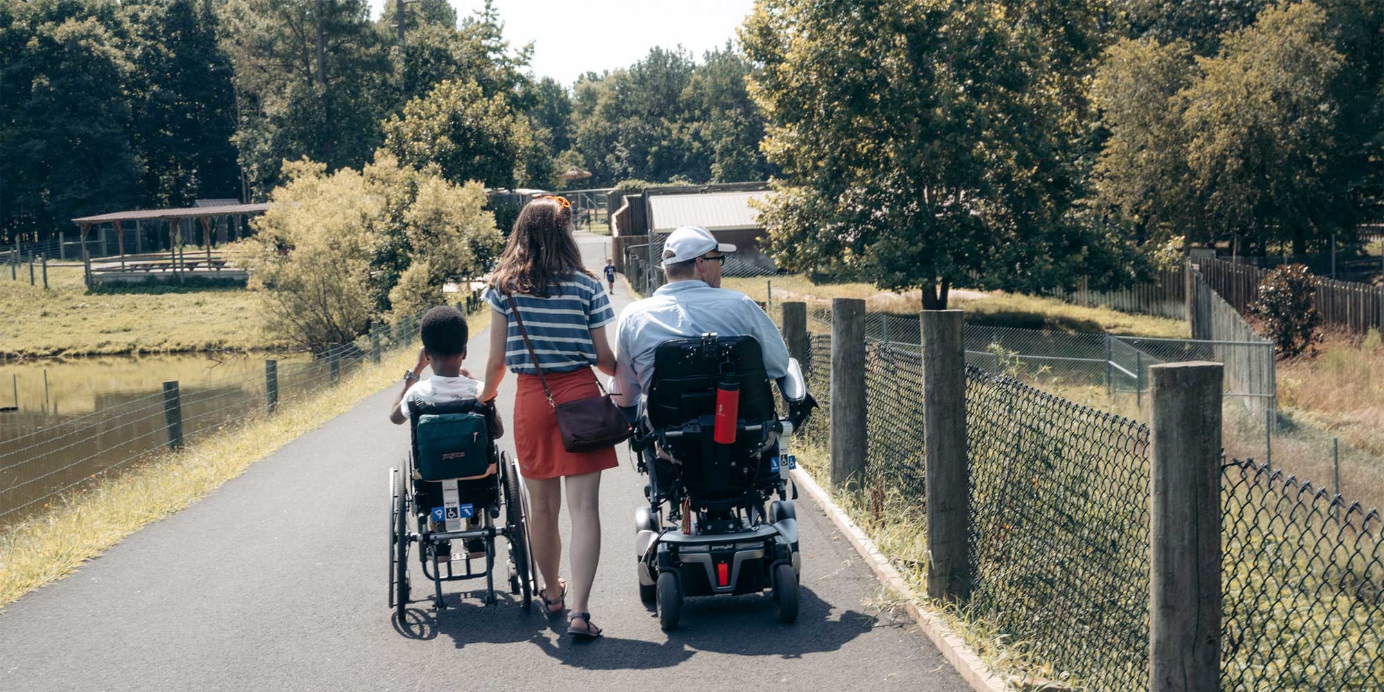 Stevie walking between John and Robert, both in their wheelchairs.