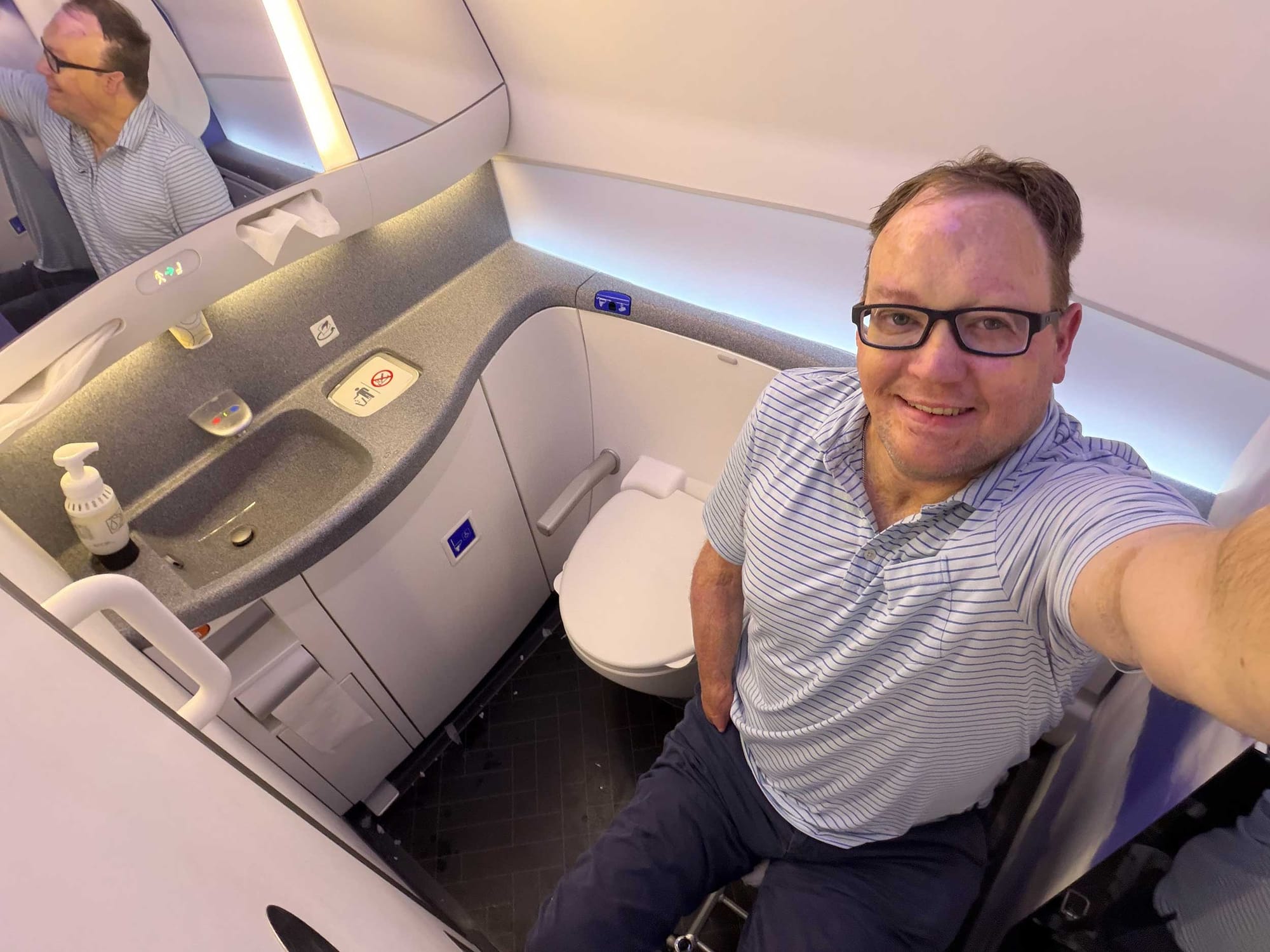 Selfie of John seated on aisle chair inside the accessible lavatory.