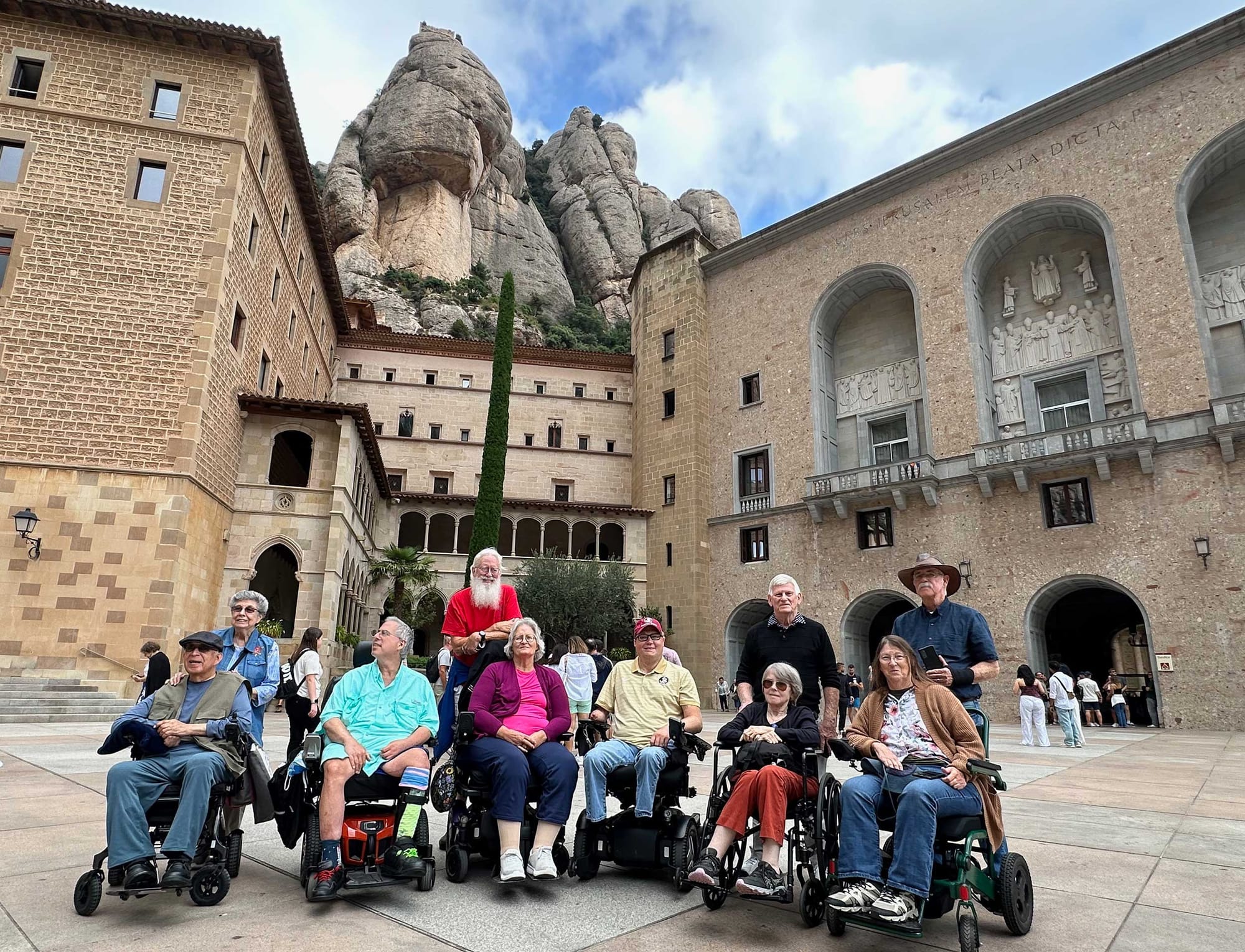 Wheelchair users in front of a mountain and monastery in Spain.