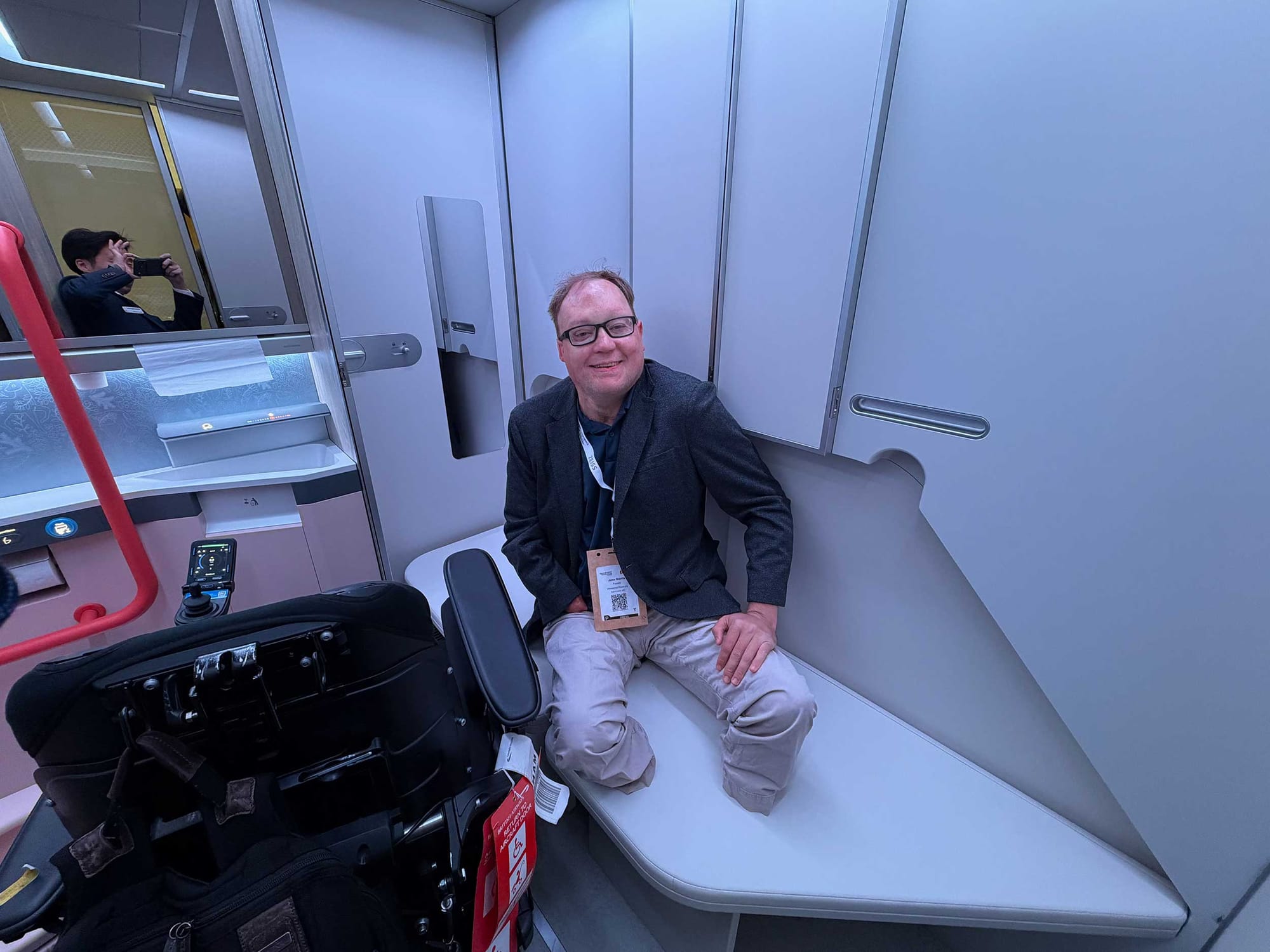 John seated on an adult changing table inside of an airplane lavatory concept.