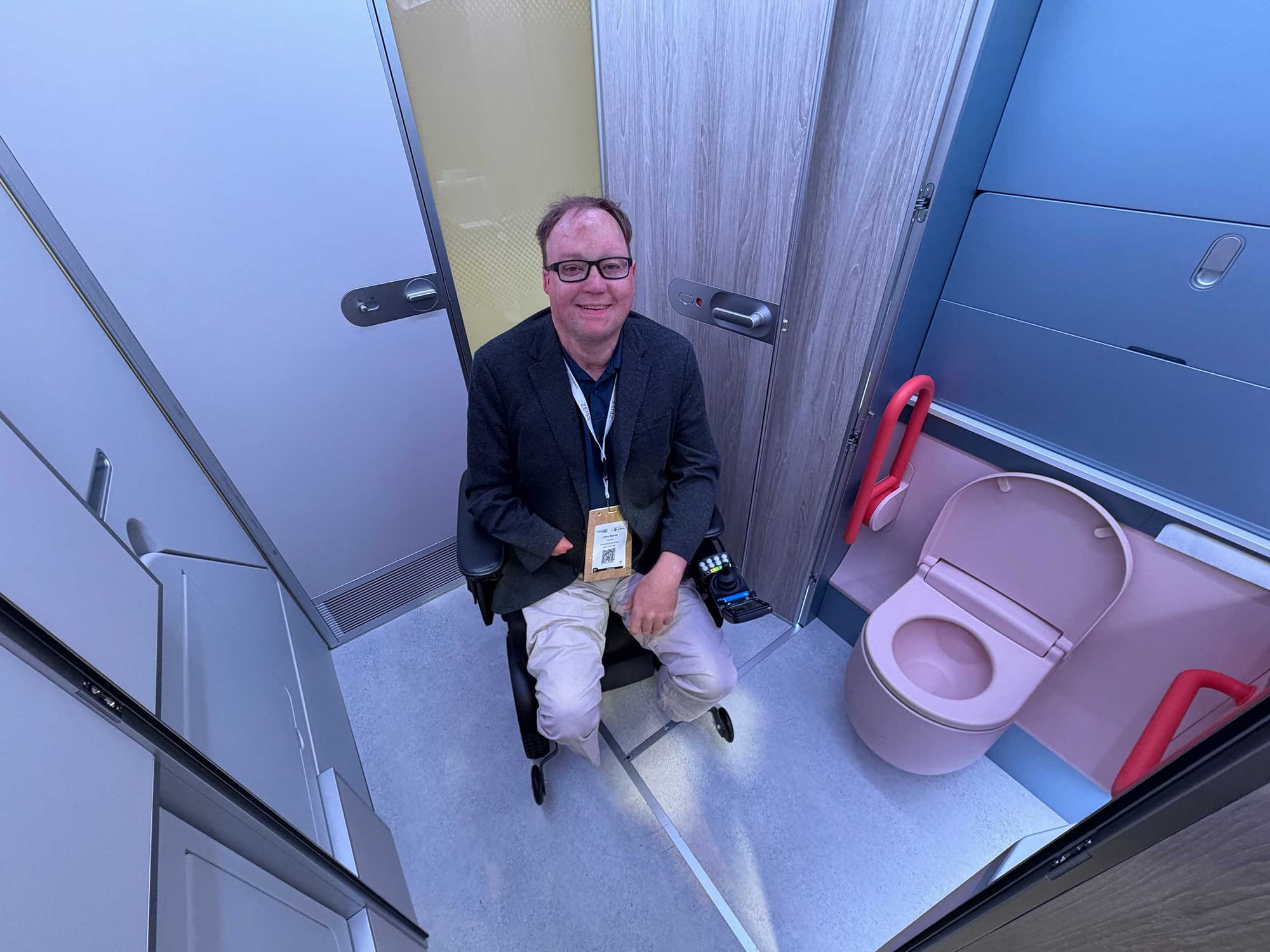 John seated in his power wheelchair inside of an airplane lavatory concept.