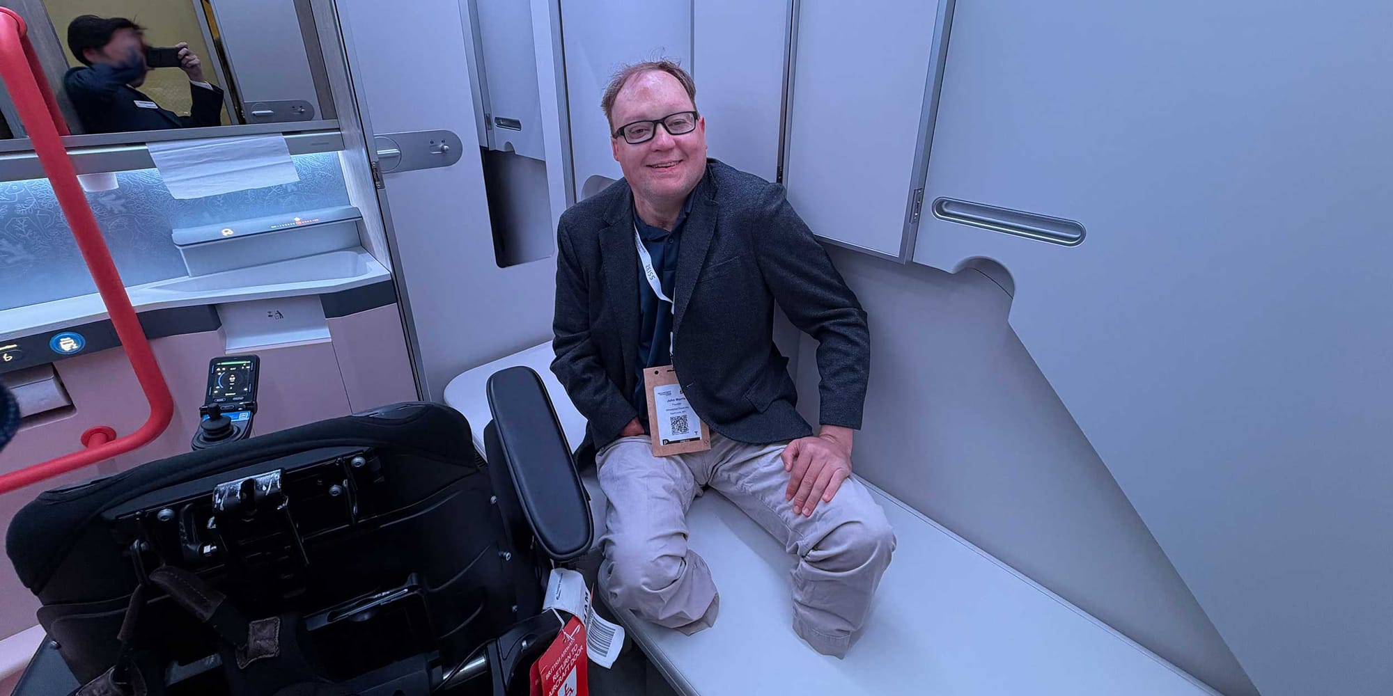 John seated on an adult-sized changing table in an airplane lavatory concept.