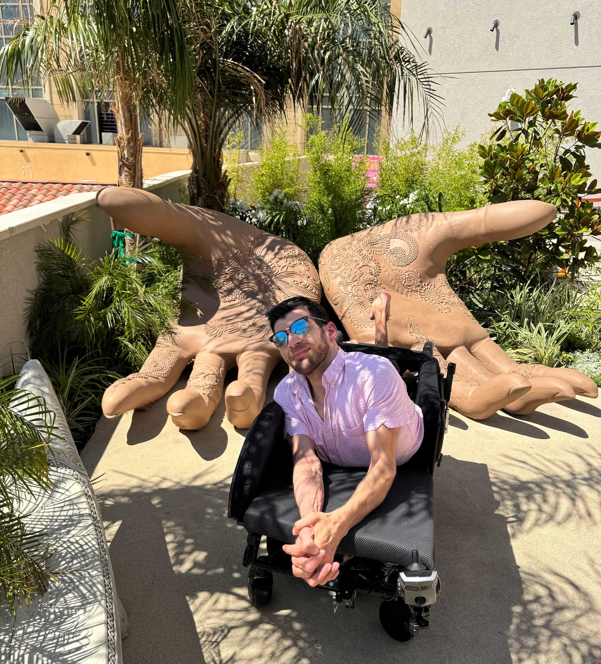 Nolan pictured in his wheelchair in front of a sculpture of two open hands.