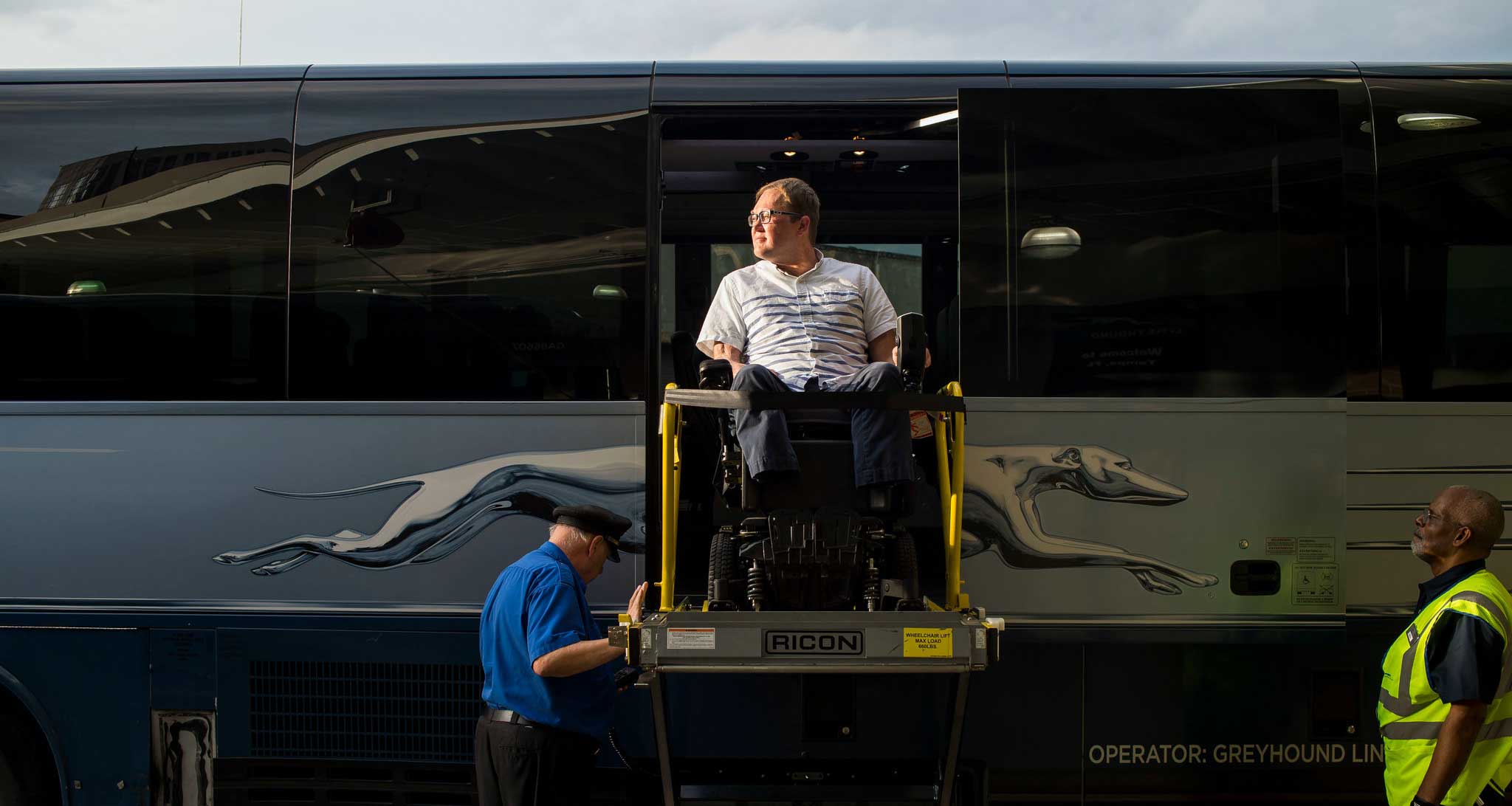 John seated in his wheelchair on Greyhound bus wheelchair lift.