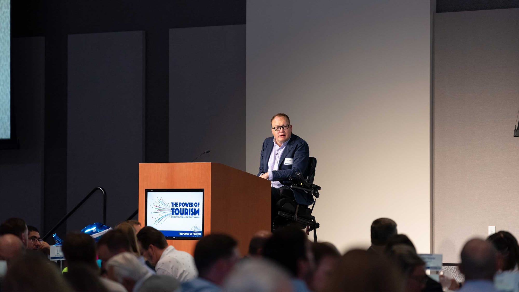 John delivering a keynote address on stage at a tourism conference.