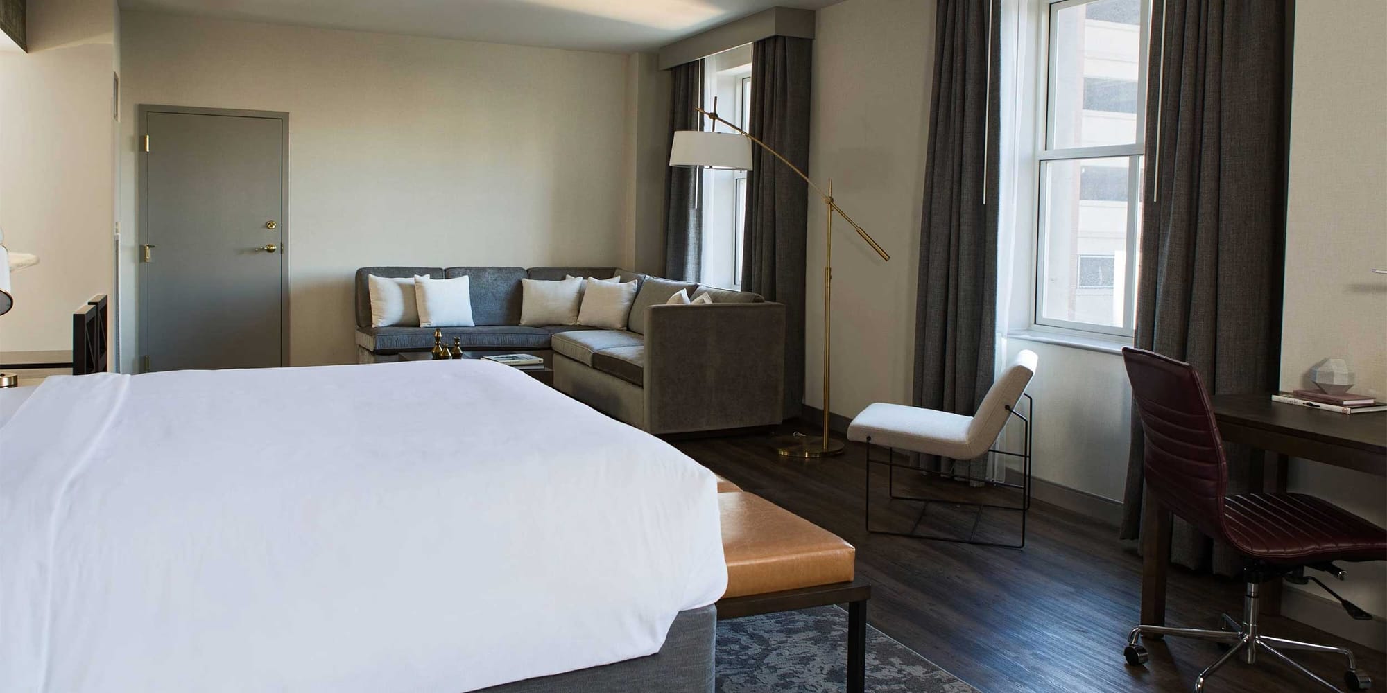 Hotel suite with king size bed, sectional sofa, desk and chair.