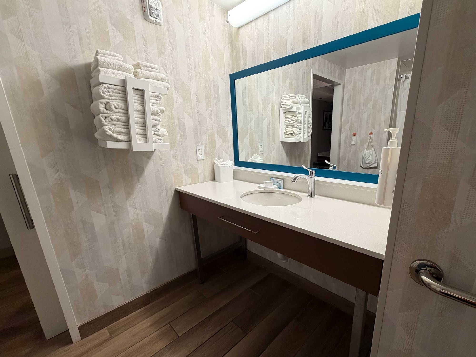Open roll-under vanity and sink, mirror and wall-mounted towel rack.