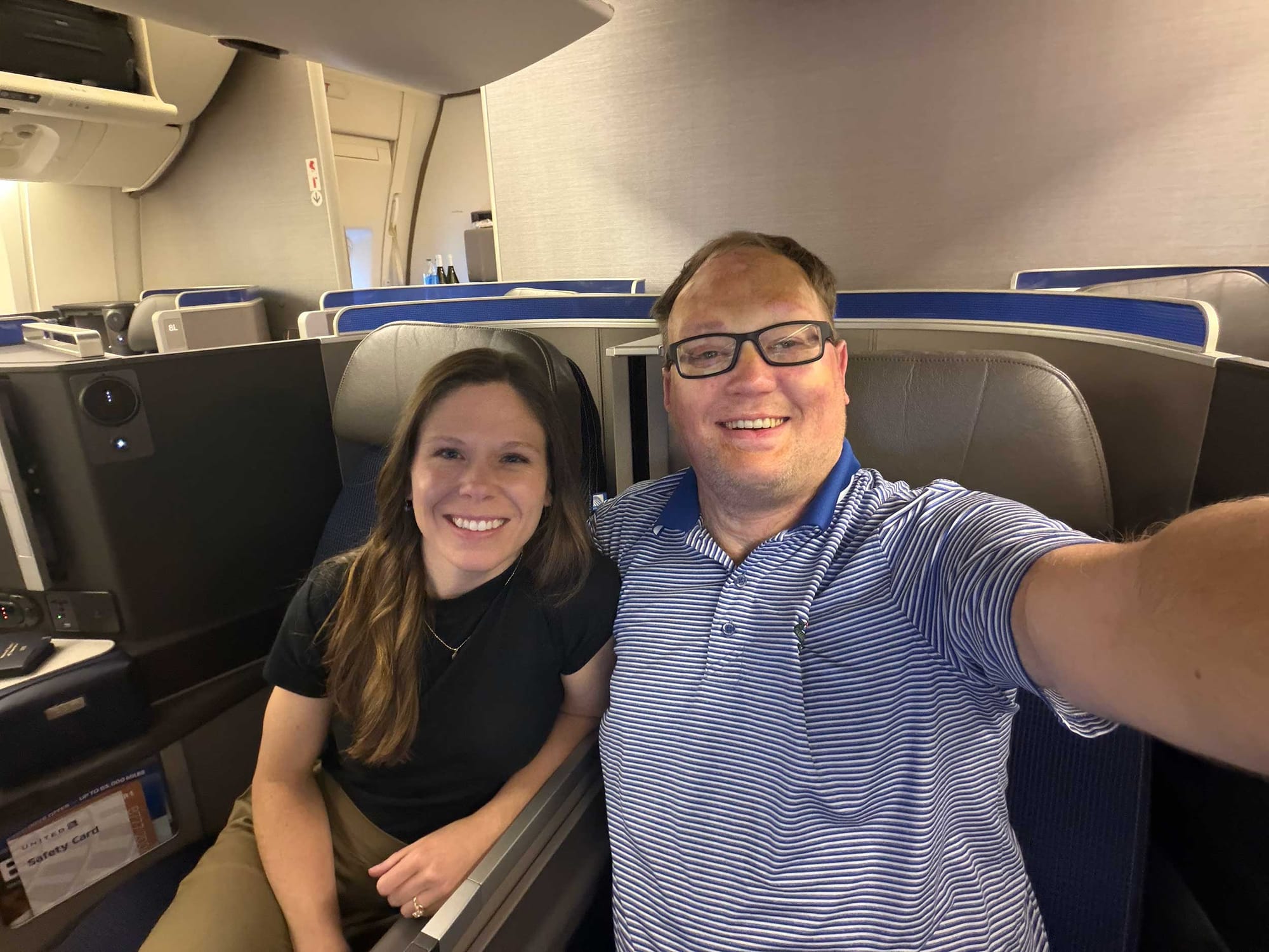 Selfie of John and Stevie sitting in a business class seat on an airplane.