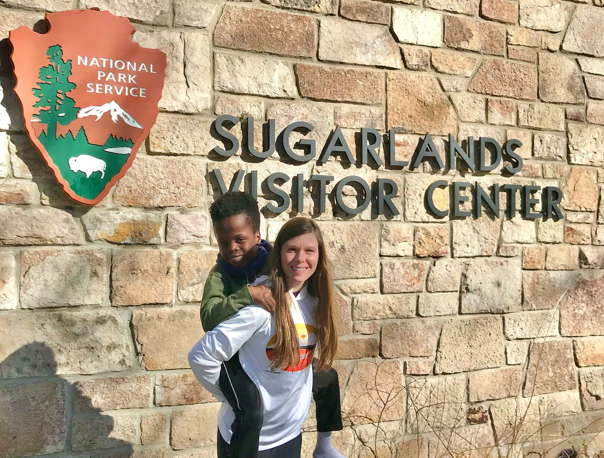 Stevie carrying Robert on her back in front of park service visitor center.