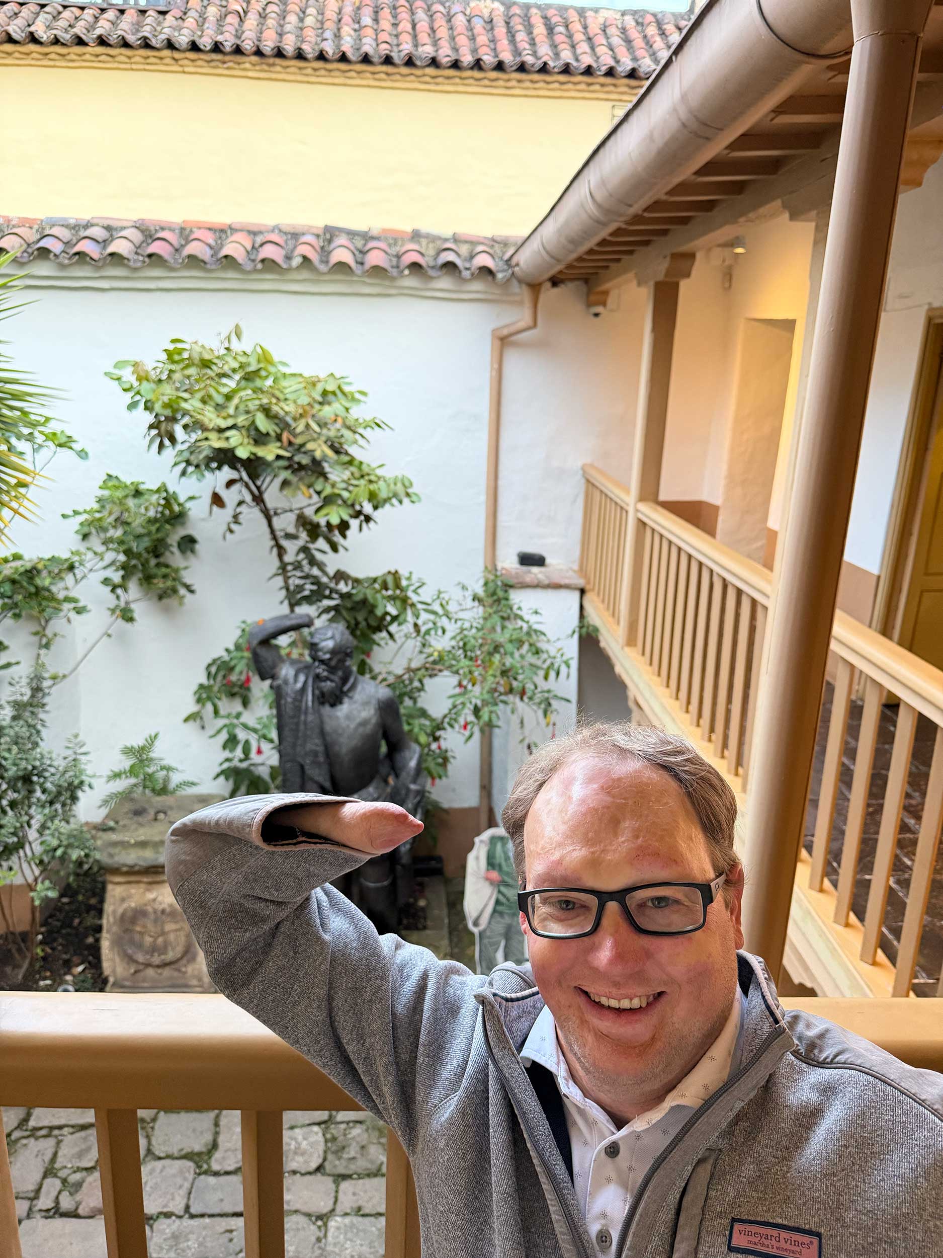 John holding his amputated right arm up in front of a statue with a similar amputation.