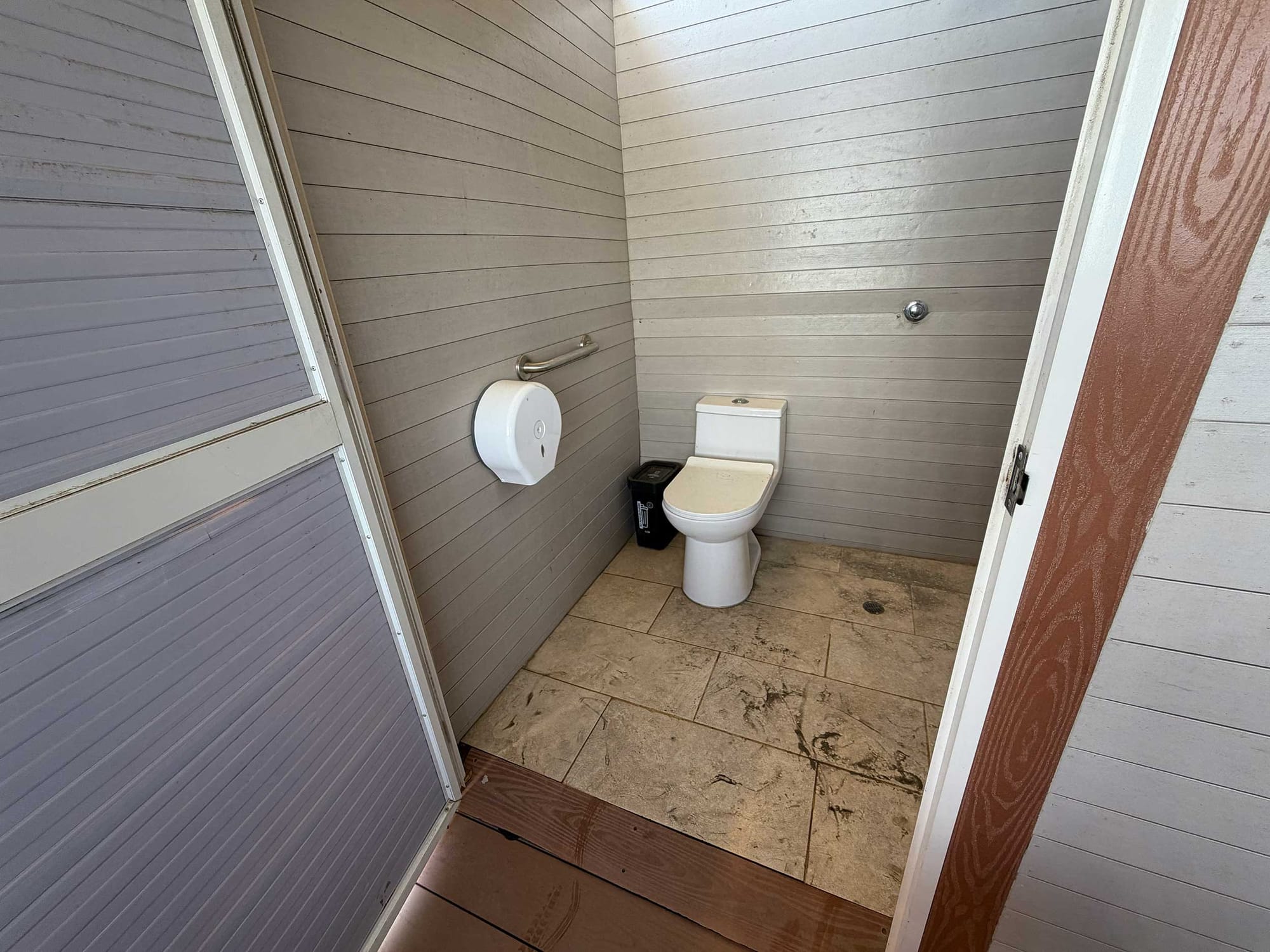 Small wheelchair accessible bathroom stall with a toilet, grab bar mounted on the wall and tile floor.