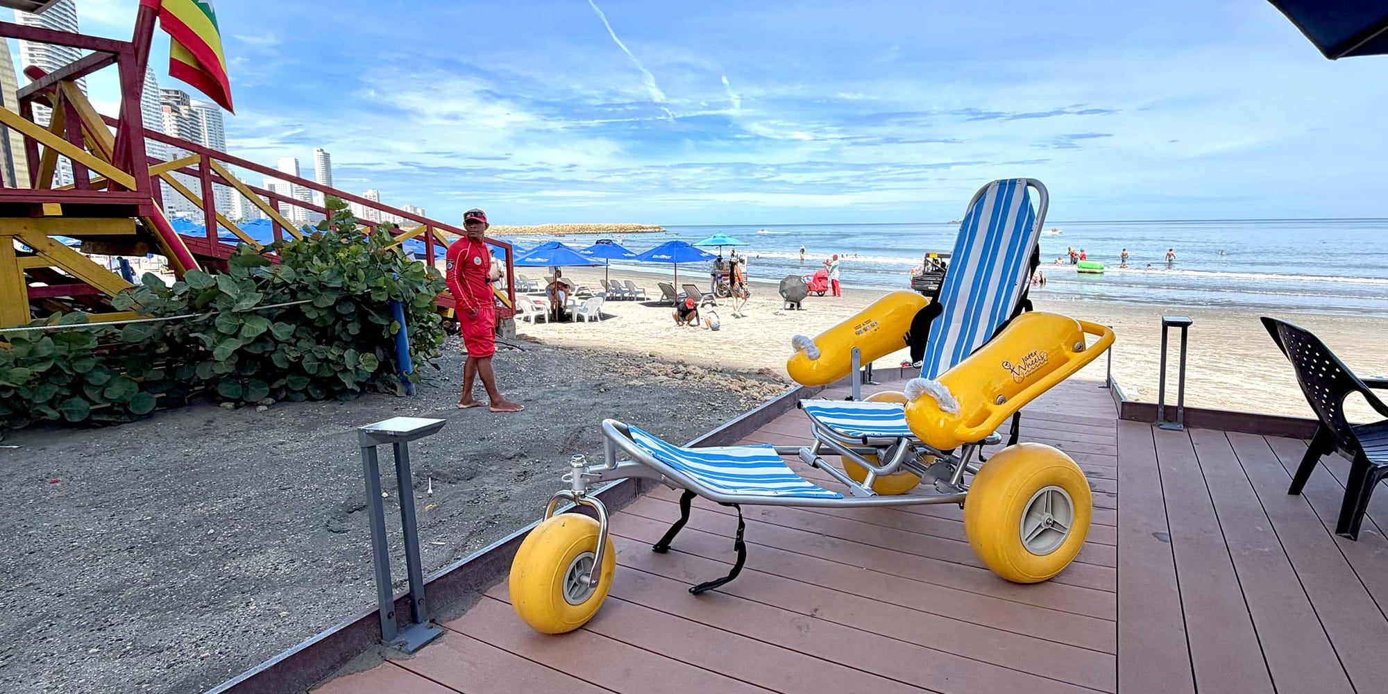 Beach wheelchair with large yellow tires on boardwalk in front of beach.
