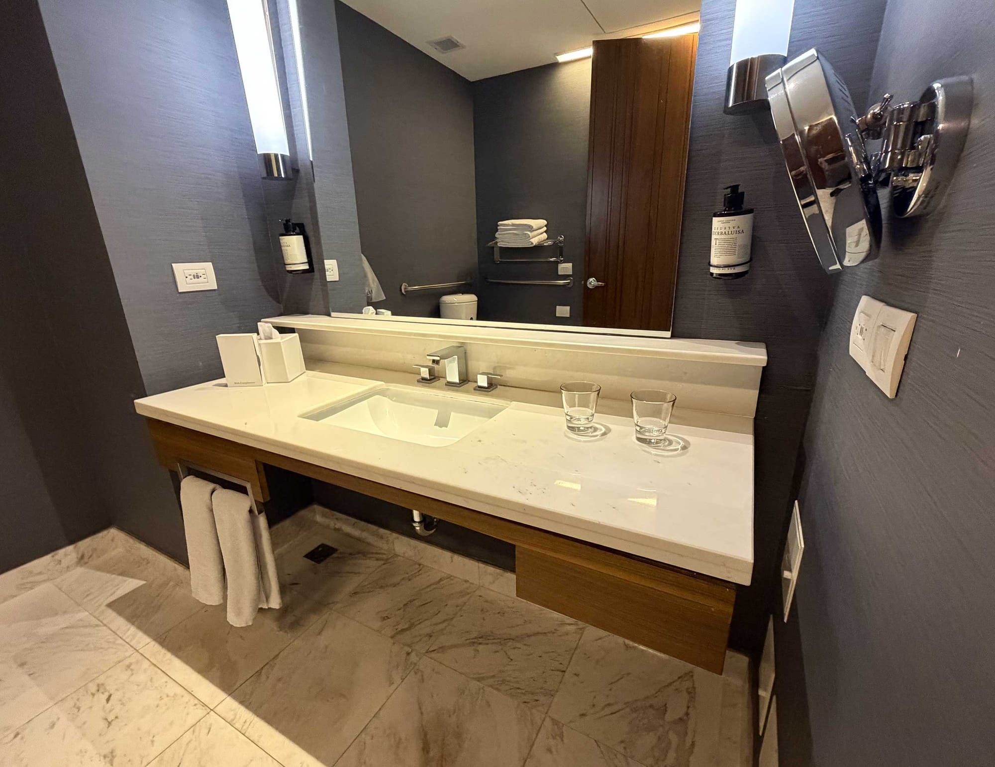 Accessible bathroom vanity with a long white marble countertop, an undermount sink, and a wood-framed open base providing roll-under space for a wheelchair.