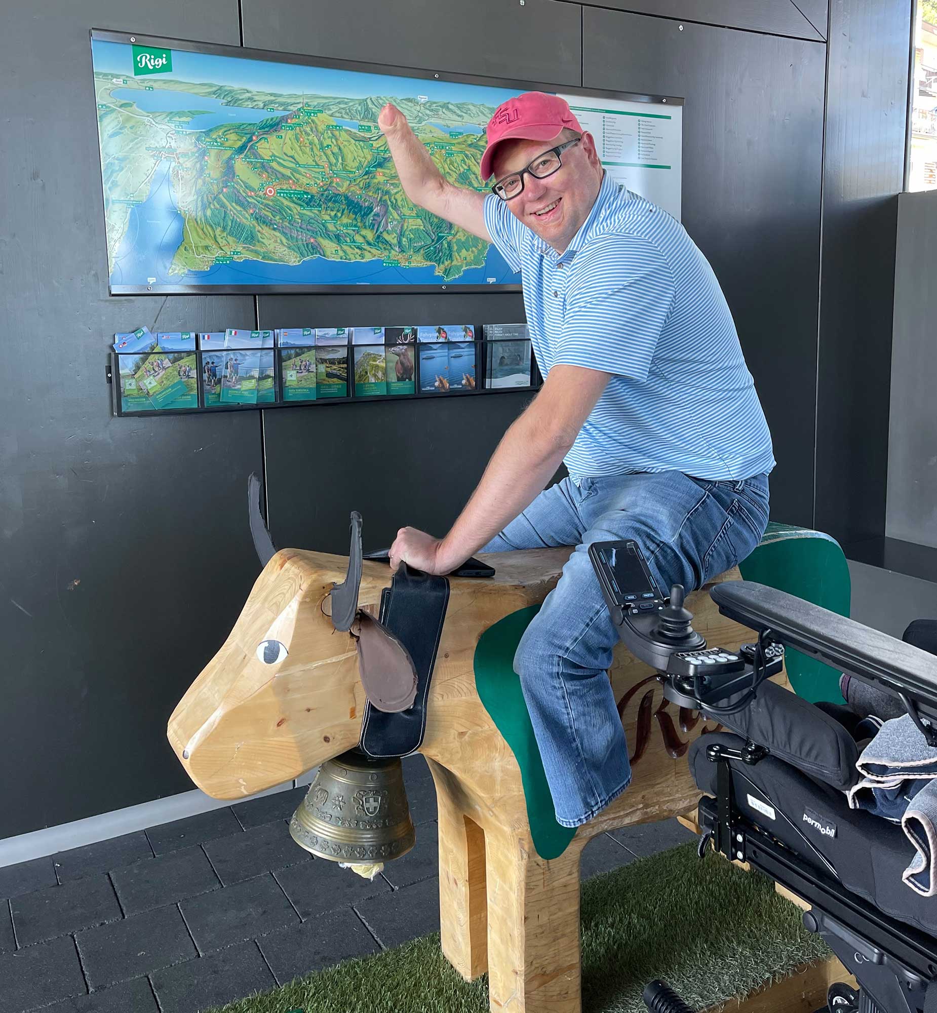 John sitting on a wooden cow acting like he is riding a bull.