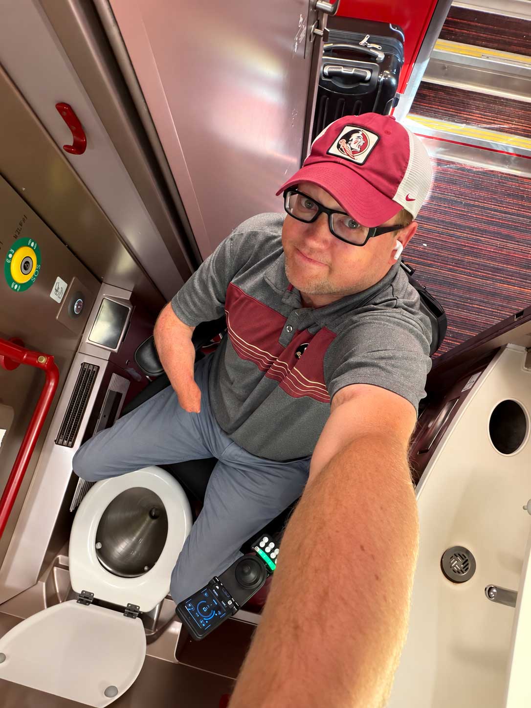 Selfie of John in his wheelchair pulled up to a toilet on a train, unable to close the door behind him.