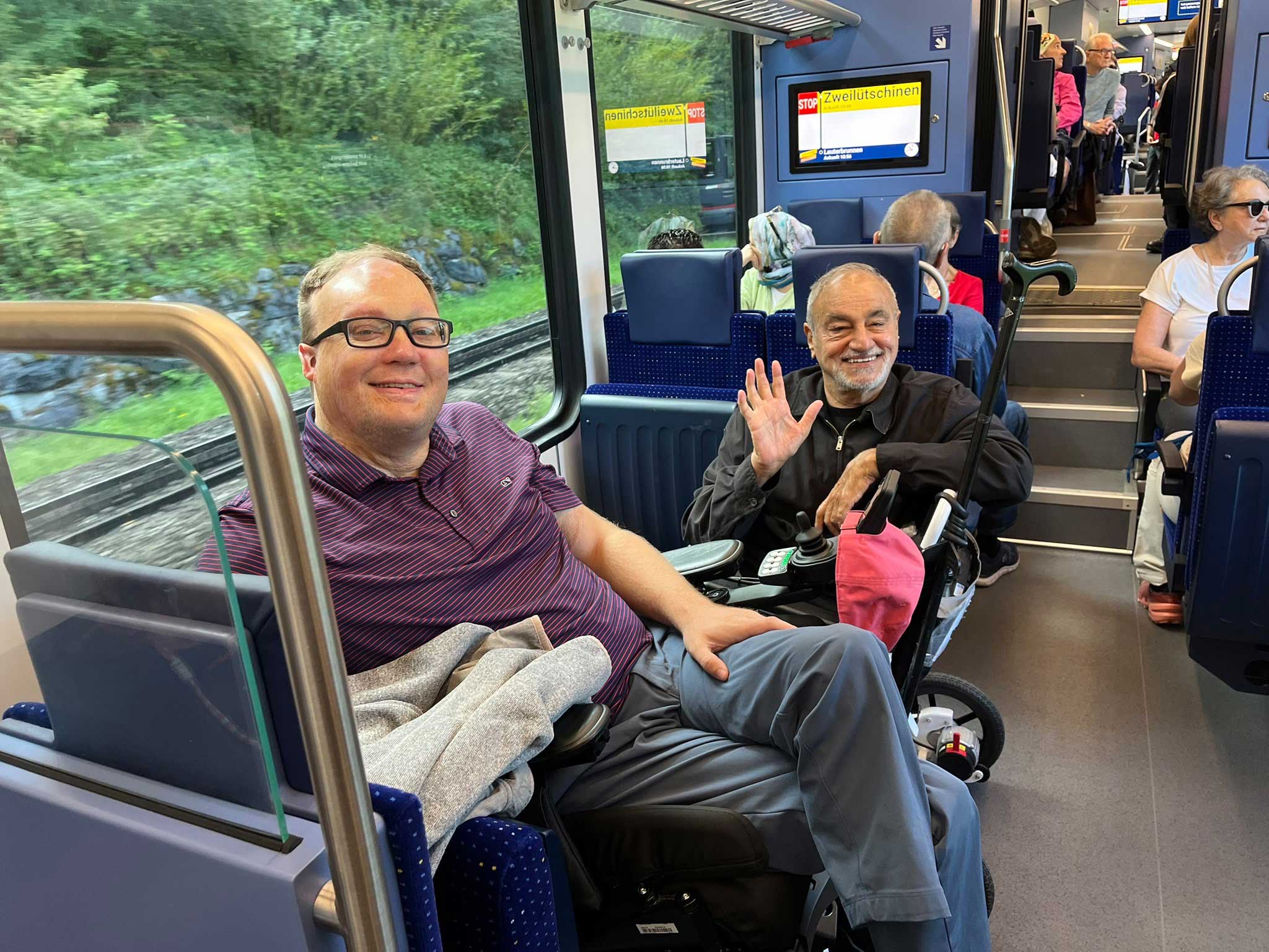 John and a fellow traveler sitting in their power wheelchairs on a Swiss train.